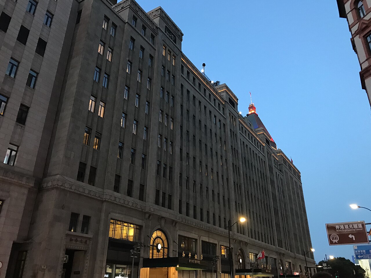 Peace Hotel’s stone facade and illuminated sign beside a Shanghai street at dusk